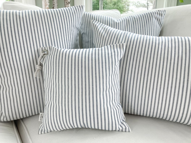 May include: Four striped throw pillows in various sizes, with a white background and blue stripes. The pillows are arranged on a white couch.
