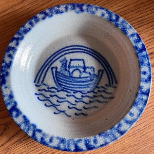 Puede incluir: Un tazón de cerámica azul y blanco con un diseño azul y blanco de un barco con un arcoíris encima. El tazón tiene un esmalte moteado.