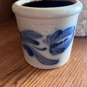 May include: A white ceramic crock with blue and white floral designs. The crock is stamped with "Westmoreland Pottery Company 1991".