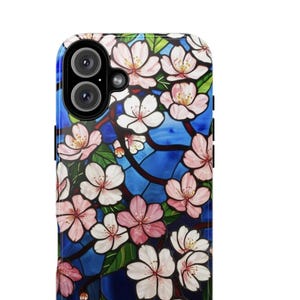 May include: A phone case with a stained-glass effect, depicting pink and white cherry blossoms against a blue backdrop. The case has a glossy finish and a camera aperture.