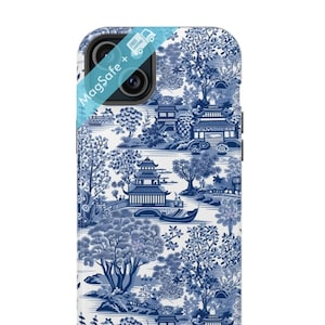 May include: A white phone case with a blue and white pattern of Chinese porcelain. The pattern features a bridge, trees, and buildings. The case has a MagSafe logo on the top left corner.