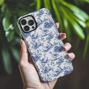 Pu&ograve; includere: Una custodia per telefono bianca con un motivo blu e bianco di anatre e fiori.