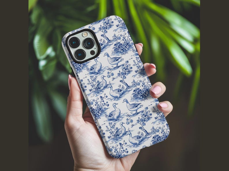 Pu&ograve; includere: Una custodia per telefono bianca con un motivo blu e bianco di anatre e fiori.