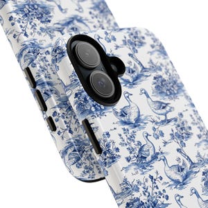 Pu&ograve; includere: Una custodia per telefono bianca con un motivo toile blu e bianco con uccelli e fiori. La custodia ha un ritaglio per l'obiettivo della fotocamera.