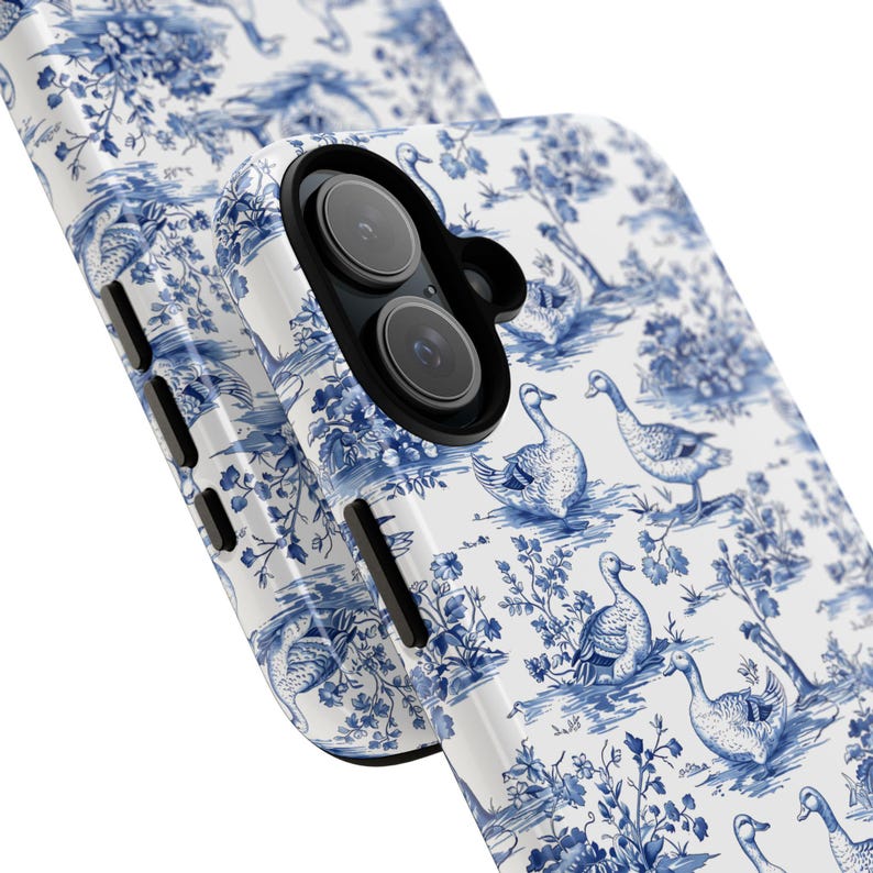 Pu&ograve; includere: Una custodia per telefono bianca con un motivo toile blu e bianco con uccelli e fiori. La custodia ha un ritaglio per l'obiettivo della fotocamera.