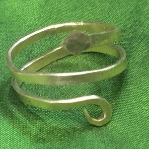 May include: A silver-toned, double-wrapped, open-ended ring with a hammered finish. The ring is made of two pieces of metal that are twisted together to form a spiral shape. The ring has a simple, minimalist design.