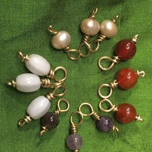 May include: A collection of eight different colored beads, including white, red, purple, and gold, strung on gold wire.