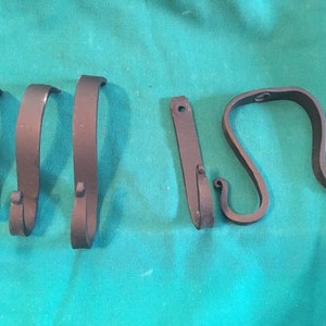 May include: Five black metal hooks with different shapes and sizes. The hooks are on a teal green surface.