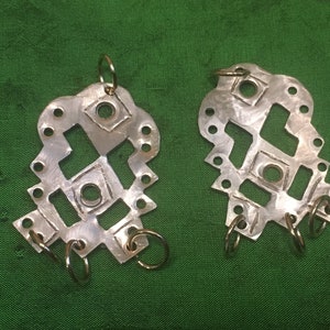 Peut inclure: Une paire de boucles d'oreilles en argent avec un motif géométrique et des anneaux dorés. Les boucles d'oreilles sont en métal et ont une finition martelée.