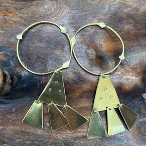 Op de afbeelding: Een paar gouden creolen met driehoekige hangers. Elke hanger heeft vijf kleinere driehoeken die eraan hangen.