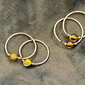 May include: Three pairs of gold hoop earrings with yellow gemstone beads.