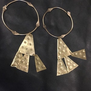 Op de afbeelding: Twee gouden metalen kettingen met driehoekige hangers. De hangers zijn gemaakt van gehamerd metaal en hebben een getextureerd oppervlak.