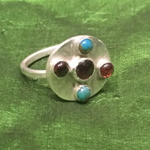 May include: A silver ring with a round face set with five stones. Three of the stones are dark red and two are turquoise.