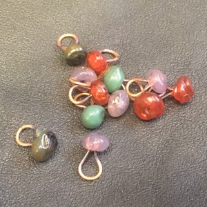May include: A group of colorful glass beads with gold metal loops. The beads are in shades of green, red, purple, and brown.