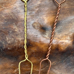 May include: Two twisted metal skewers, one gold and one copper, with a loop at the top and two prongs at the bottom.