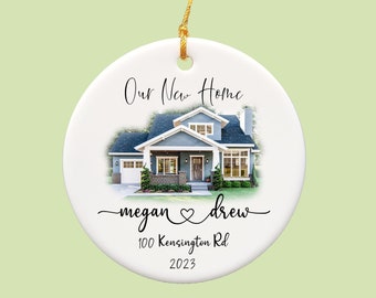 May include: A white ceramic ornament with a watercolor illustration of a blue house. The text "Our New Home" is above the house, with names and an address below. A gold string is attached for hanging.