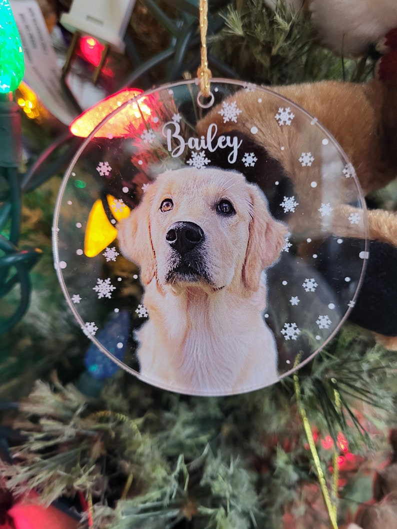 Clear Round Acrylic Christmas ornament with a photo of a dog and name with snow flakes background.