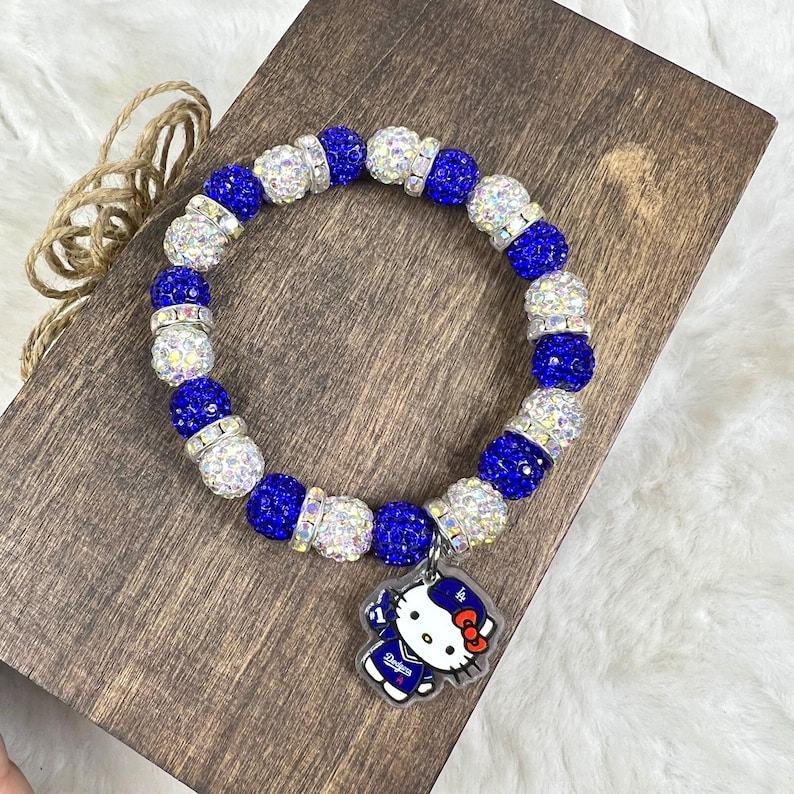 May include: A blue and silver beaded bracelet with a charm featuring a cartoon character in a baseball uniform. The bracelet has alternating blue and silver beads. The charm has the word "Dodgers" on it.