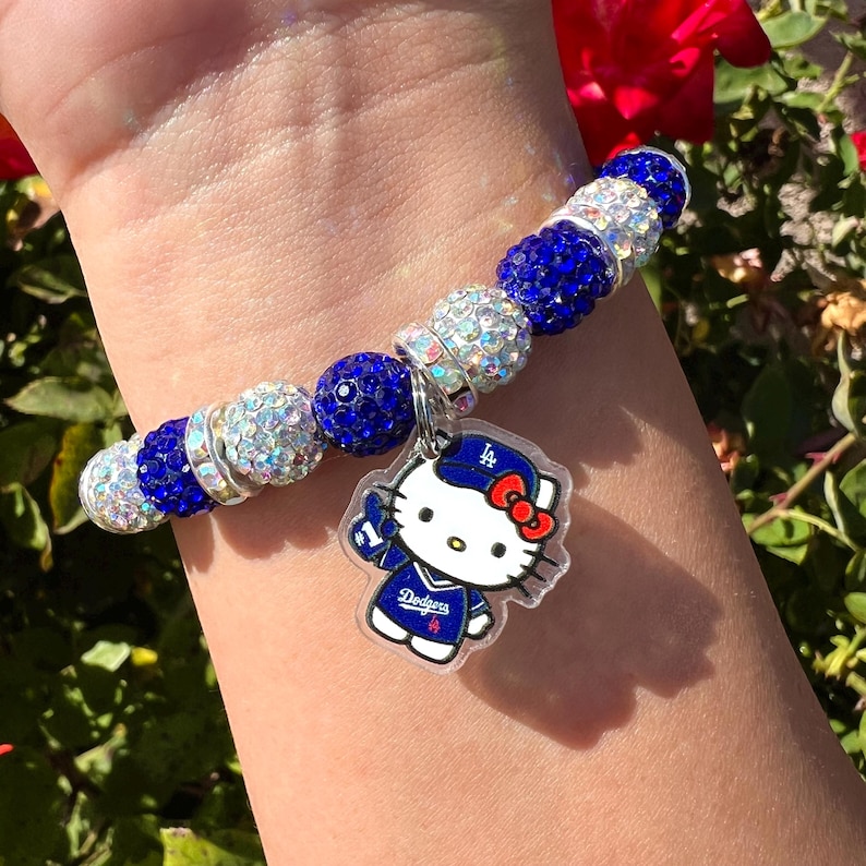 May include: A bracelet with blue and silver beads, and a charm of Hello Kitty in a Dodgers baseball uniform. The bracelet features a mix of round and faceted beads.