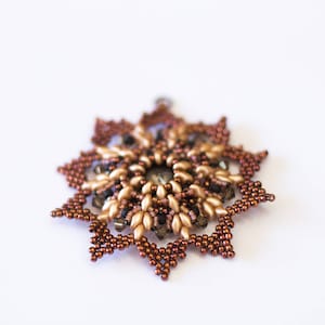 Op de afbeelding: Een bruine en gouden kralen sneeuwvlok ornament met een kristal in het midden.