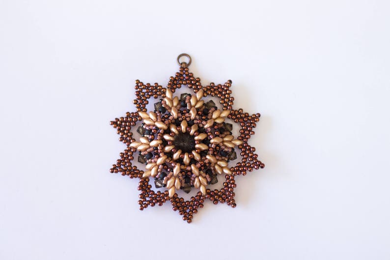 Op de afbeelding: Een bruine en gouden kralen sneeuwvlok ornament met een metalen lus om op te hangen.