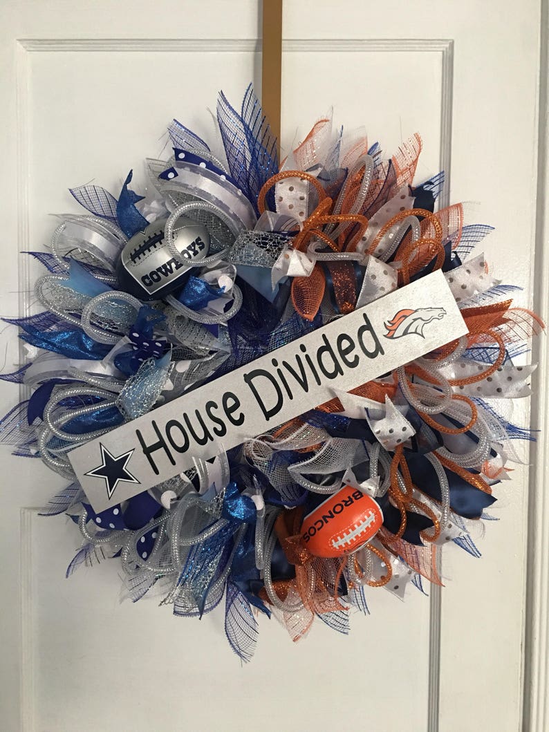 Puede incluir: Una corona decorativa con cintas azules, plateadas y naranjas, con adornos tem&aacute;ticos de f&uacute;tbol americano. La corona tiene un letrero que dice "House Divided" con logotipos de equipos y un bal&oacute;n de f&uacute;tbol. Un art&iacute;culo de decoraci&oacute;n festiva.