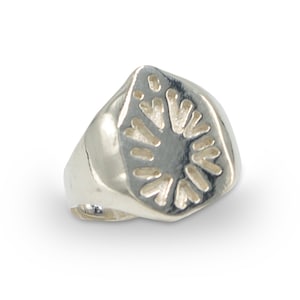 May include: A silver ring with a geometric design on the top. The design is a circle with a series of small triangles radiating outward from the center.