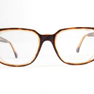 May include: Rectangular eyeglasses with a tortoiseshell pattern on the frames. The lenses are clear, and the temples are a light brown color. The glasses have a vintage aesthetic and are set against a white background.