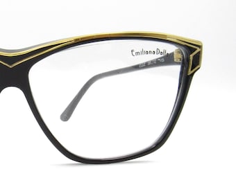 May include: Close-up of a pair of black eyeglasses with a gold trim. The glasses have a cat-eye shape with clear lenses. The brand name "Emiliana Dalla" is printed on the lens.