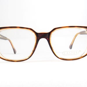 May include: Vintage eyeglasses with a tortoiseshell pattern frame. The rectangular frames have a dark brown color with a lighter brown and clear rim. The lenses are clear, and the temples are a light brown color.