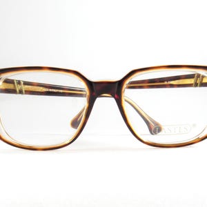 May include: Rectangular eyeglasses with a tortoiseshell pattern frame. The glasses have clear lenses and a brown and gold color scheme. The brand name "LASTES" is visible on the lens. The frame is made in Italy.