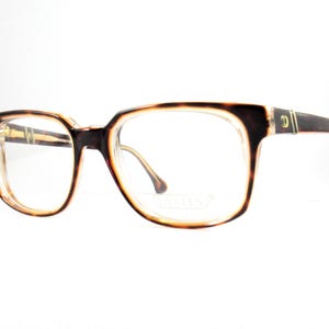 May include: Eyeglasses with a tortoiseshell pattern on the frames. The frames have a rectangular shape with rounded edges. The lenses are clear. The temples are dark brown with a gold accent. The overall style is vintage.
