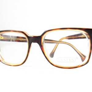 May include: Vintage eyeglasses with a tortoiseshell pattern on the frames. The glasses have a rectangular shape with clear lenses and gold-toned arms. The brand name "LASTES" is visible on the lenses.