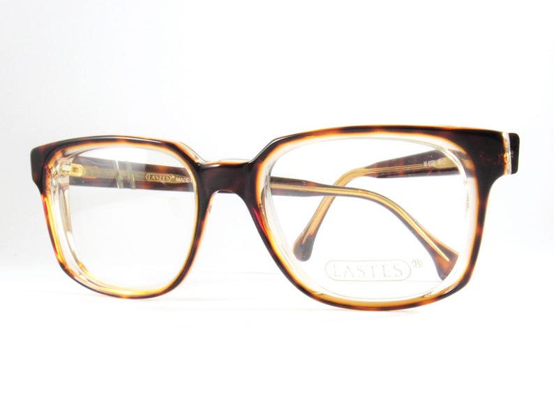 May include: Vintage eyeglasses with a tortoiseshell pattern on the frames. The glasses have a rectangular shape with clear lenses and gold-toned arms. The brand name "LASTES" is visible on the lenses.