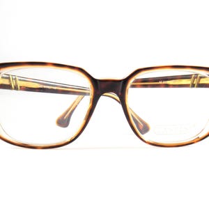 May include: Vintage eyeglasses with a tortoiseshell pattern frame. The rectangular frames have a clear lens and a brown and tan color scheme. The arms and bridge of the glasses are a light brown color. The glasses are set against a white background.