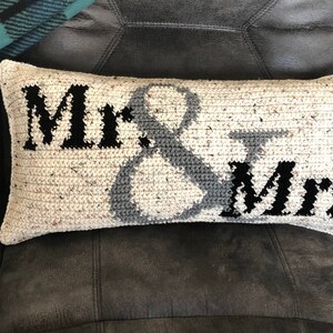 May include: A white crocheted pillow with the words "Mr. & Mrs." in black and gray lettering.