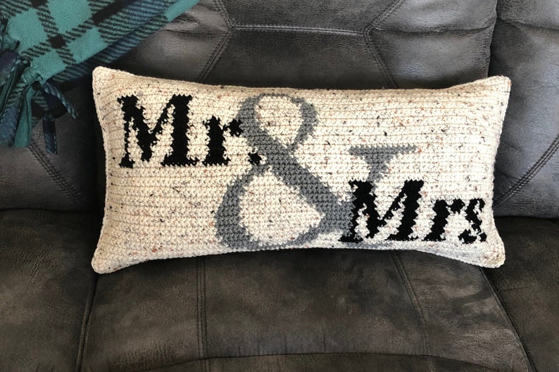 May include: A white crocheted pillow with the words "Mr. & Mrs." in black and gray lettering.
