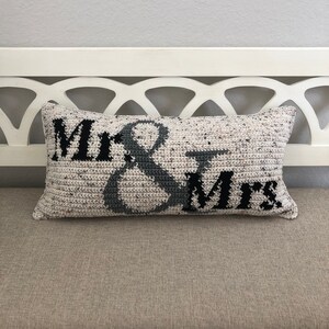 May include: A white and gray crocheted pillow with the words "Mr. & Mrs." in black lettering.