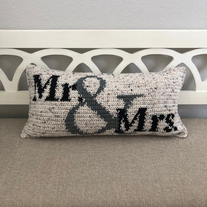 May include: A white and gray crocheted pillow with the words "Mr. & Mrs." in black lettering.