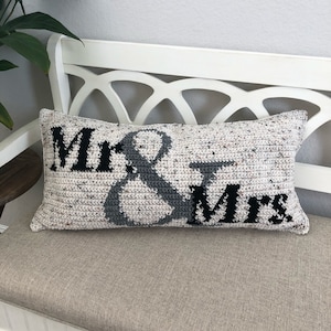 May include: A white and gray crocheted pillow with the words "Mr. & Mrs." in black lettering.
