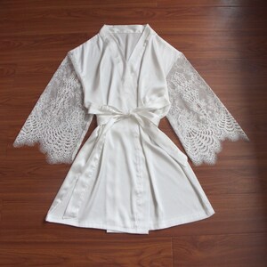 May include: White satin robe with lace sleeves. The robe has a tie belt and a V-neck.