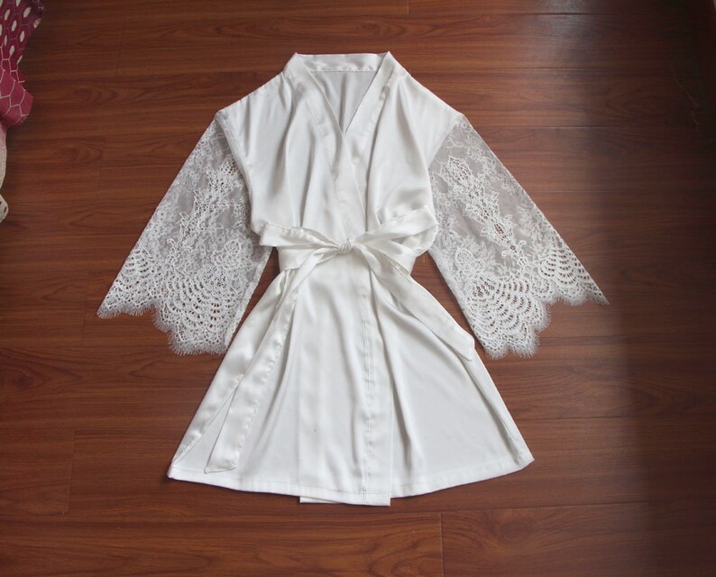 May include: White satin robe with lace sleeves. The robe has a tie belt and a V-neck.