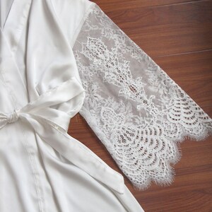 May include: A white satin robe with lace sleeves. The robe has a tie at the waist and is made of a soft, luxurious fabric.