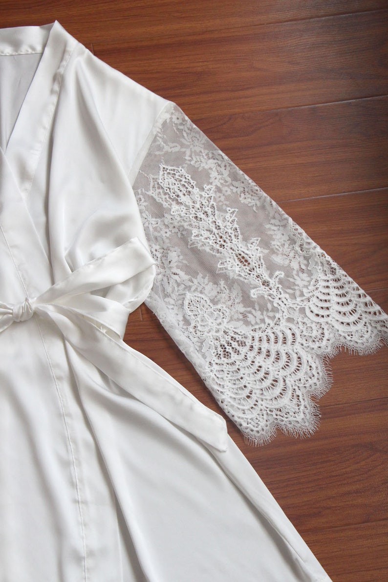 May include: A white satin robe with lace sleeves. The robe has a tie at the waist and is made of a soft, luxurious fabric.