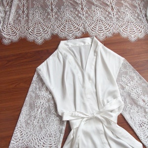 May include: White satin robe with lace sleeves. The robe has a V-neck and a tie belt.