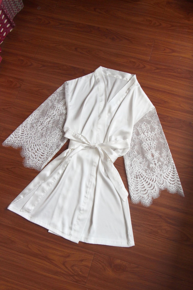 May include: White satin robe with lace sleeves. The robe has a tie belt and a V-neck.