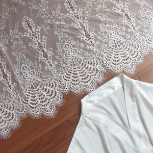 May include: White satin robe with lace trim. The robe has a V-neck and long sleeves. The lace trim is delicate and intricate.