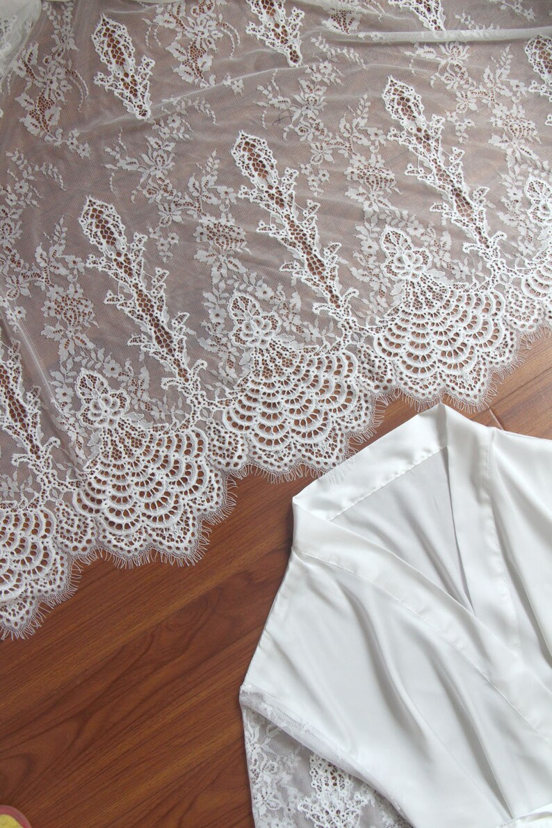 May include: White satin robe with lace trim. The robe has a V-neck and long sleeves. The lace trim is delicate and intricate.