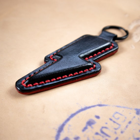 Hand-stitched leather keychain with a bold lightning bolt design in black and red — the kind of small everyday carry piece that feels custom, not catalog.