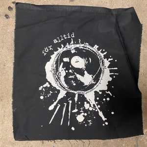 May include: Black fabric patch with a white design. The design features a person's face inside a circle of barbed wire, with the text "för alltid" above the circle. There are also white splatter marks and nails around the circle.